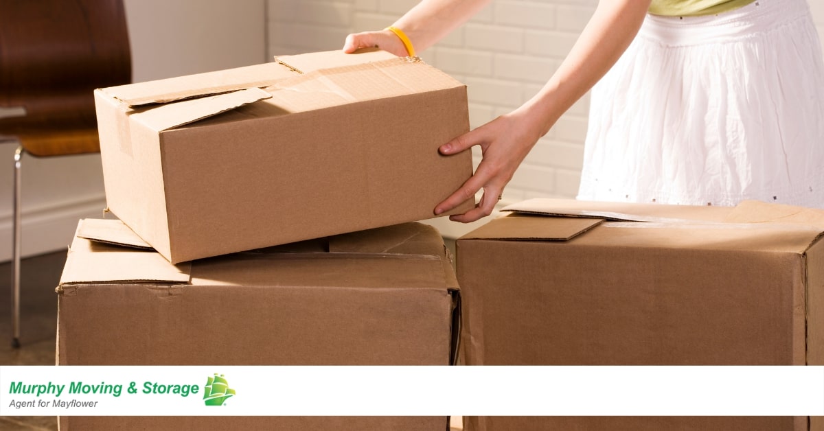 A person putting a closed cardboard box on top of other cardboard boxes