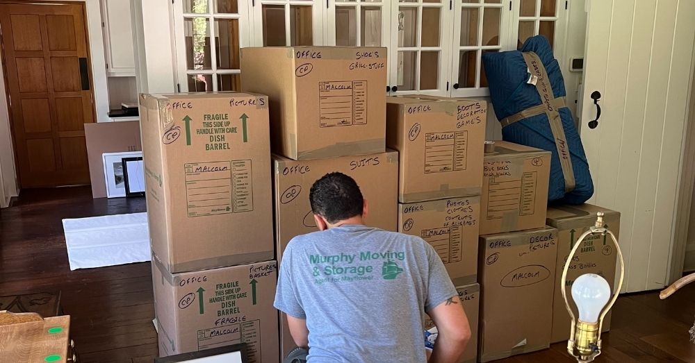 A mover from Murphy Moving & Storage is organizing stacked moving boxes in a room.