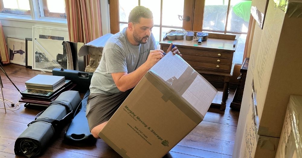 A mover kneels to label a box with a marker.