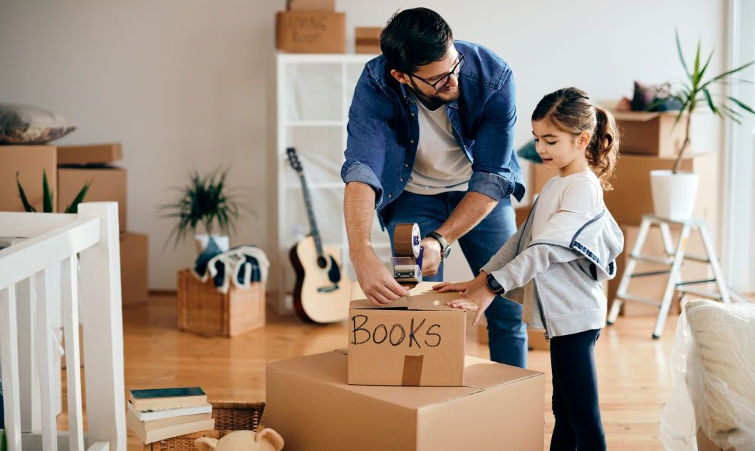 Happy little girl with her father packing her books for home relocation