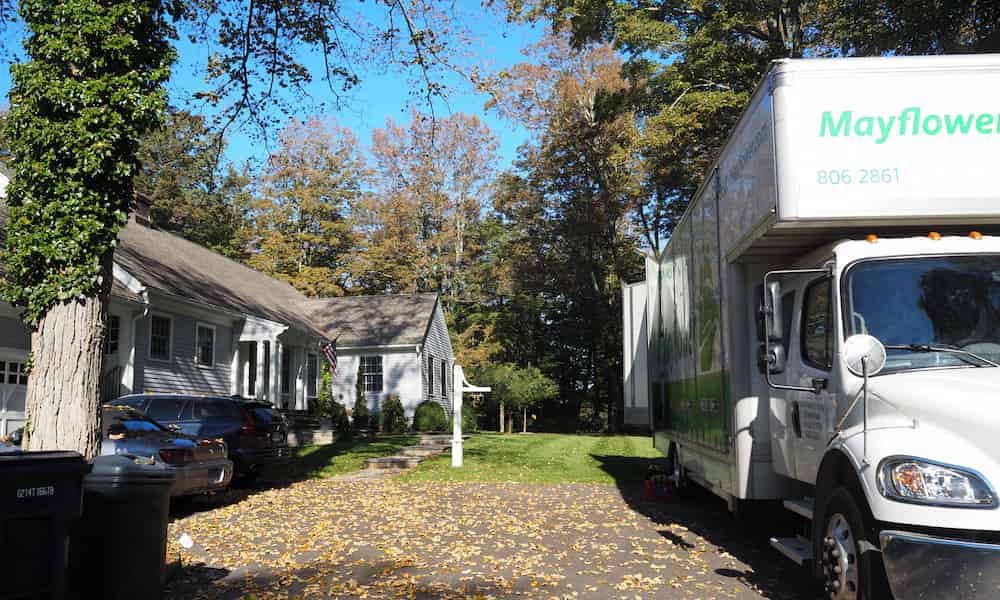Moving truck parked outside suburban house with driveway and trees