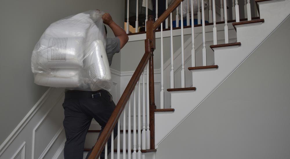 Mover moving up from stairs carrying packed mattress