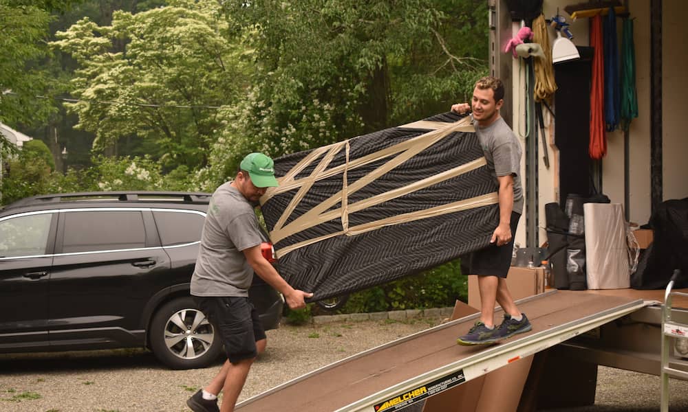 Movers carrying a wrapped TV into a moving truck