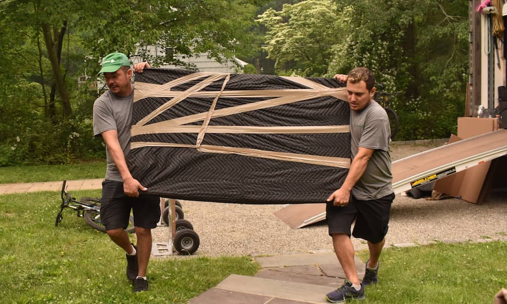Movers carrying a wrapped household items for smart house relocation