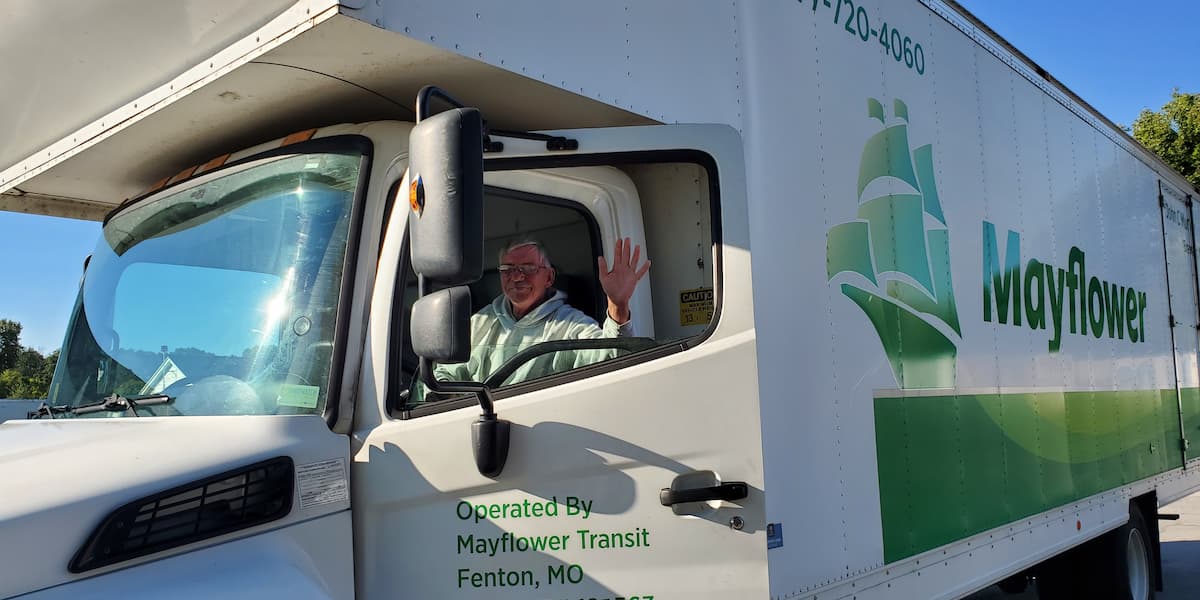 Senior customer waving from inside a Mayflower moving truck on a sunny day