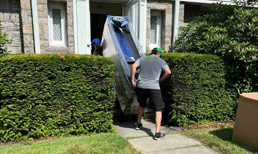 Two movers carefully maneuvering a large, wrapped piece of furniture