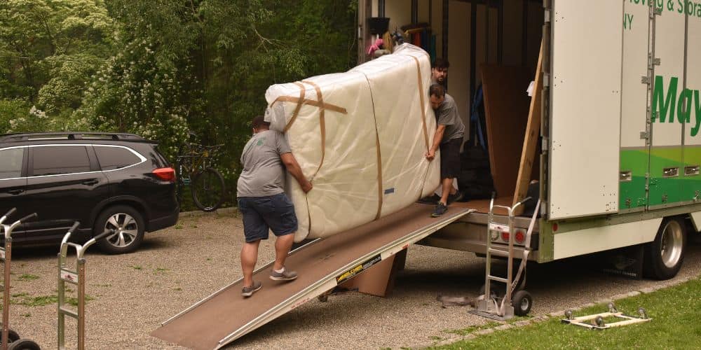 Two professional movers carrying a large mattress wrapped in protective plastic