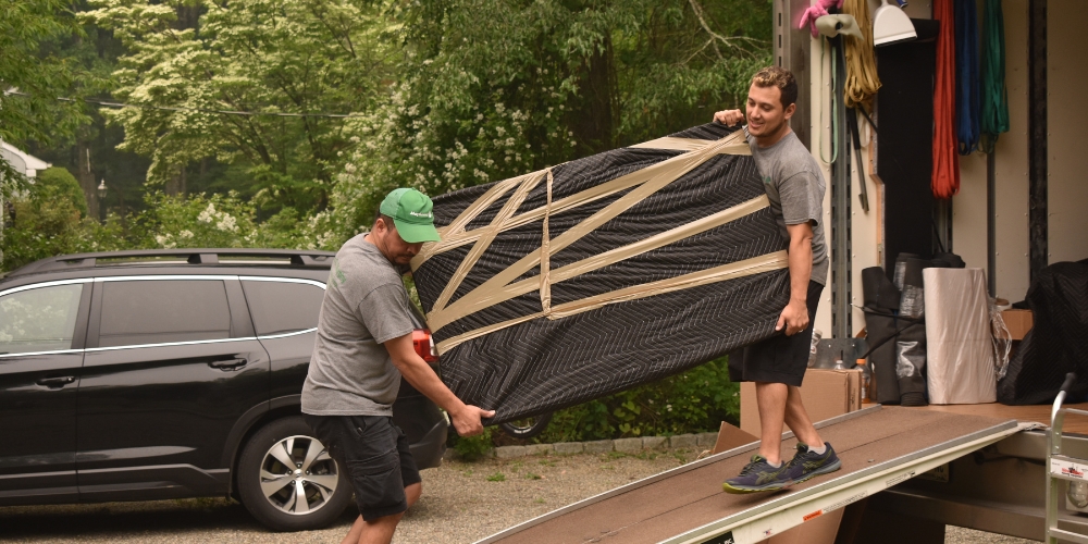 Two movers carefully carrying a large piece of furniture
