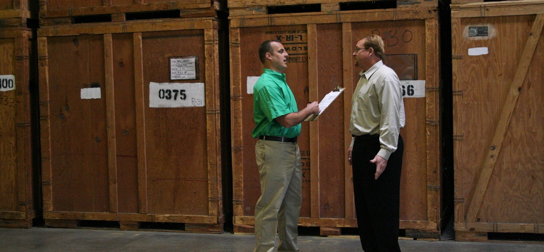 Two men converse near large wooden crates inside a storage warehouse