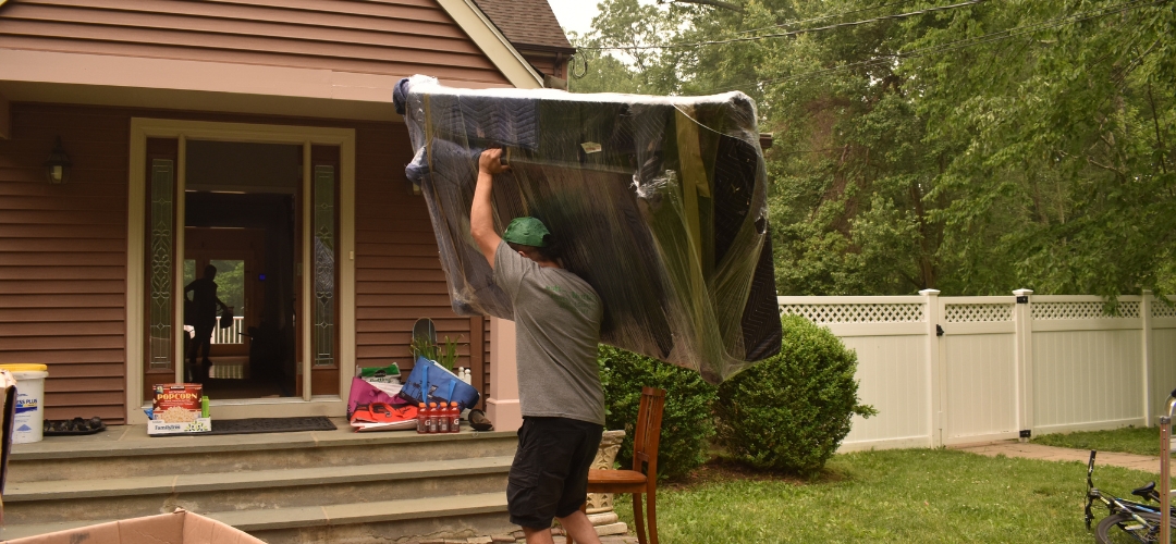 A mover carrying a large, plastic-wrapped piece of furniture