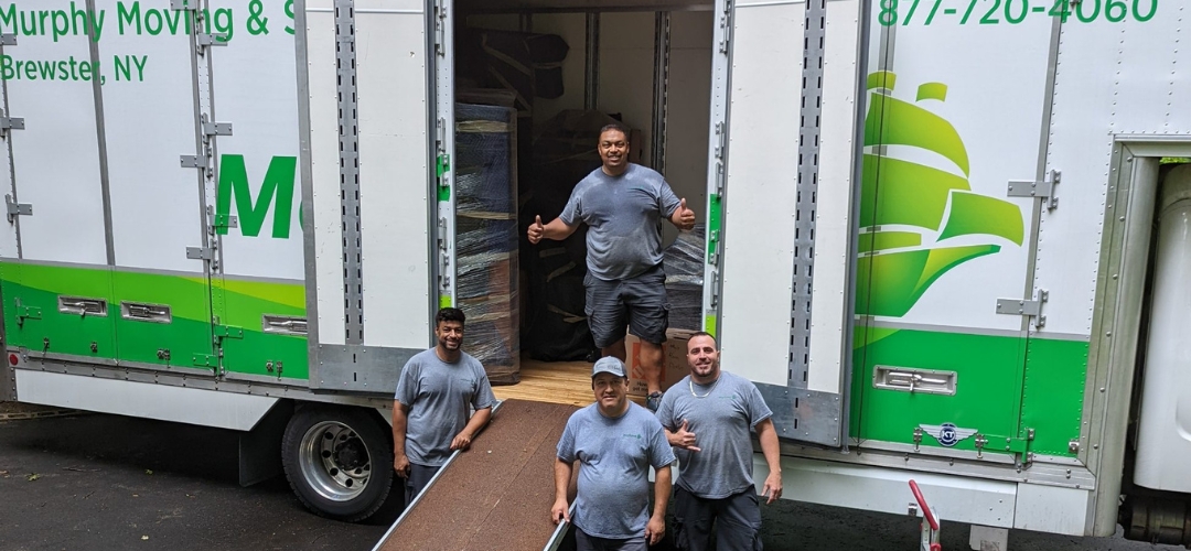 Four smiling moving company workers posing by the open rear doors