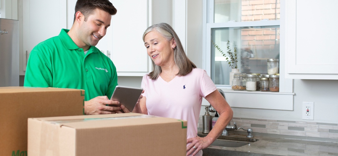 A Mayflower mover in a green polo shirt showing a digital tablet to a woman