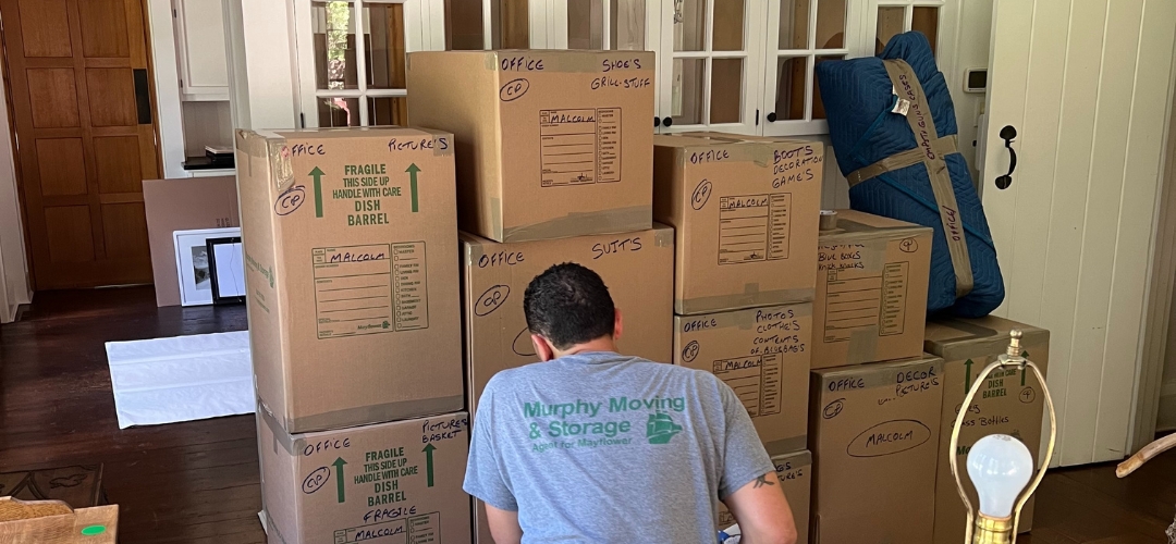 A Murphy Moving & Storage worker stands before a stack of labeled cardboard