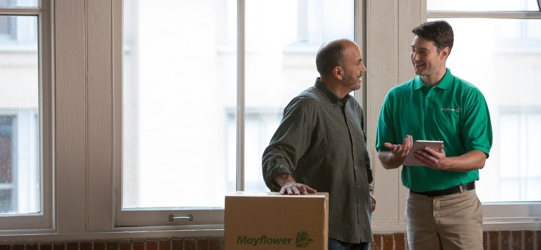 A man leaning on a Mayflower box talks with a smiling mover