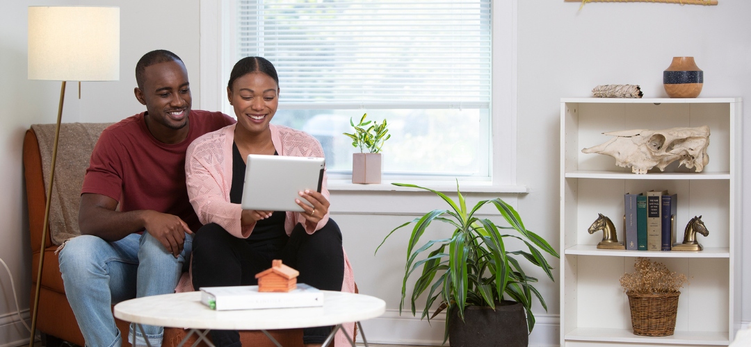 A smiling couple sits together in a bright living room