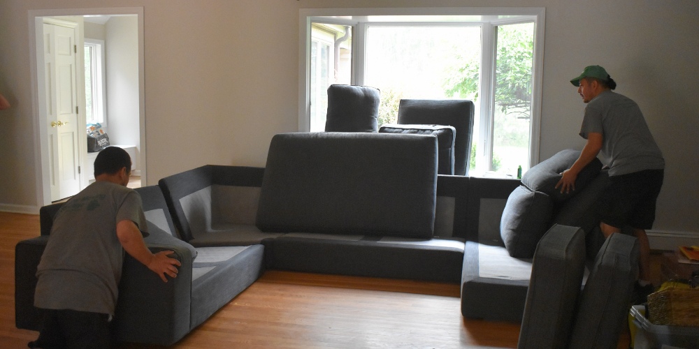 Two movers assembling or arranging a large sectional sofa