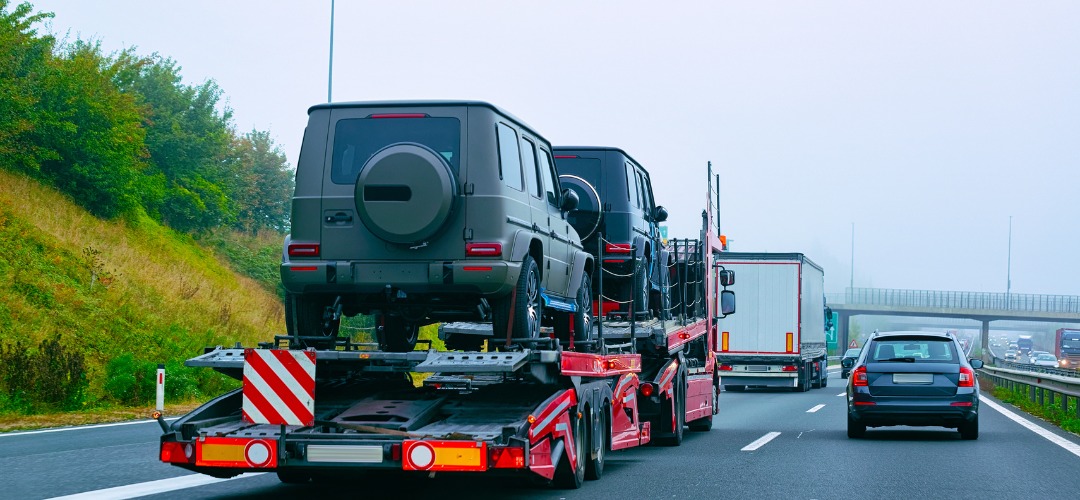 A car carrier on a highway loaded with two matte black luxury SUVs
