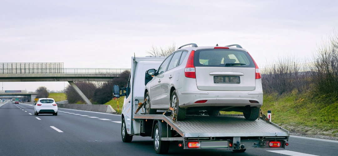 A white flatbed tow truck transporting a silver station wagon