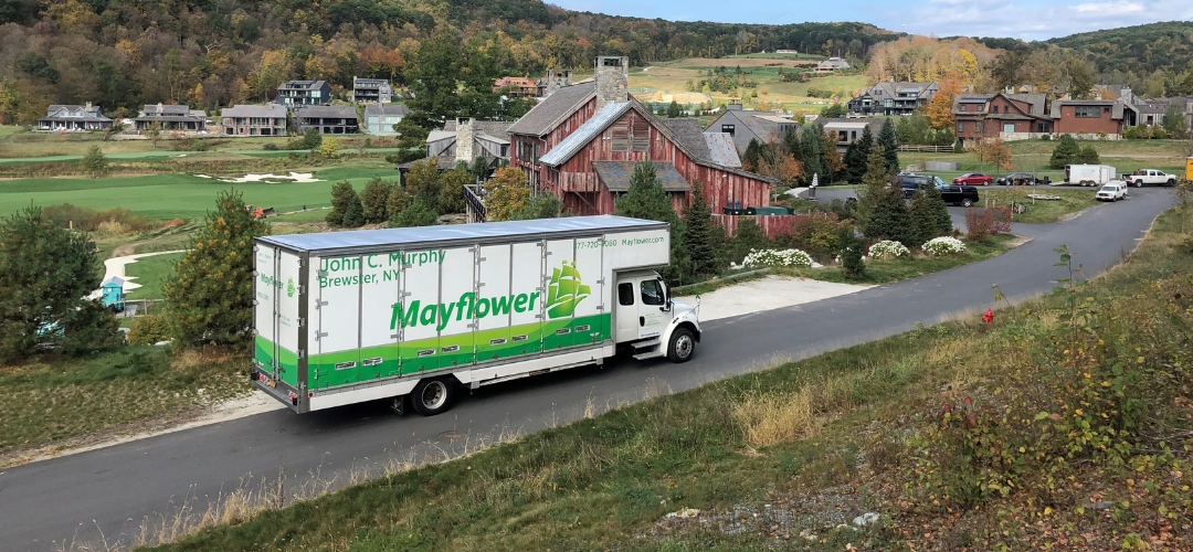 A moving truck drives along a paved road near a residential neighborhood