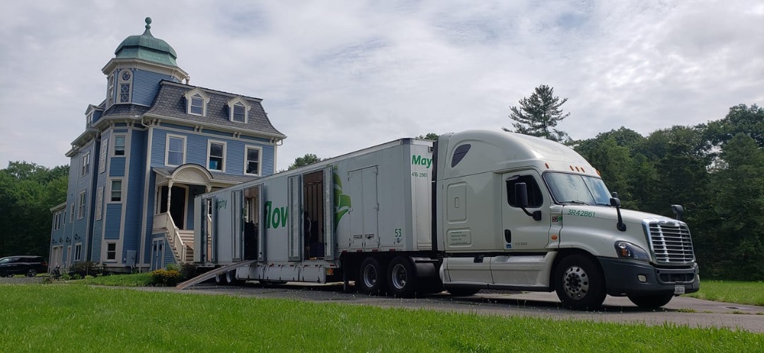 a moving trailer parked outside a historic blue Victorian building