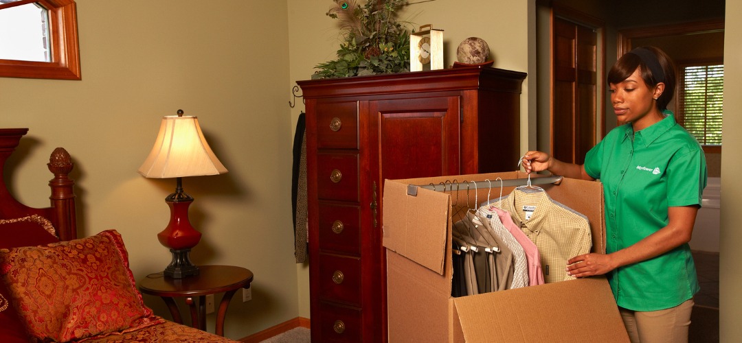 female mover in a green shirt packing hanging clothes