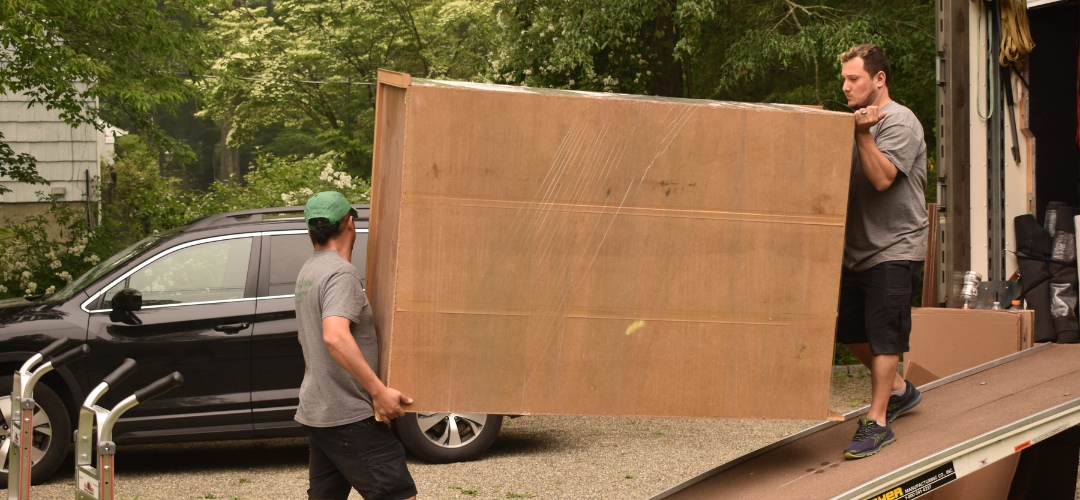 Two movers carry a large, cardboard-wrapped piece of furniture