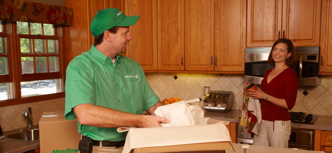a mover in a green uniform packs kitchen items into a cardboard box