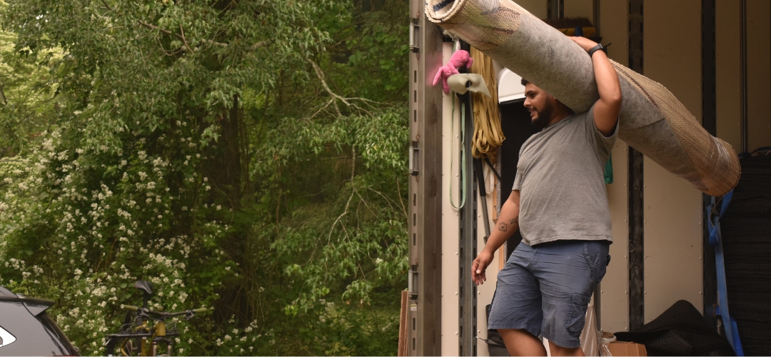 carrying a large, rolled-up rug on his shoulder