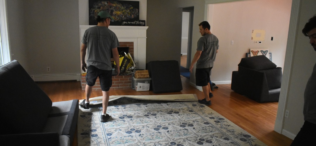 Two men carry a large, plastic-wrapped mattress
