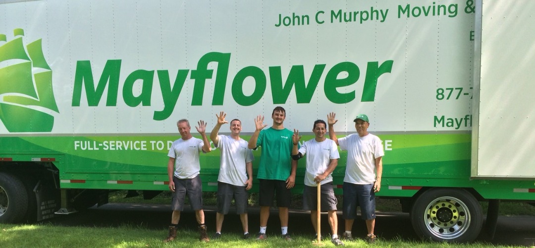 Five movers waving in front of a green and white Mayflower moving truck