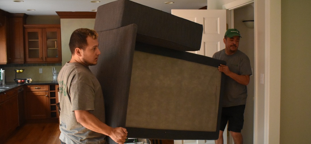 two movers carrying a dark sofa