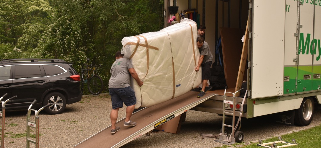 Movers loading a large mattress up a truck ramp
