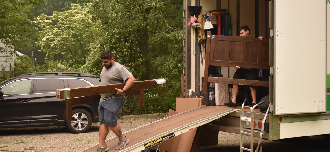 Movers loading a wooden bed frame onto a truck