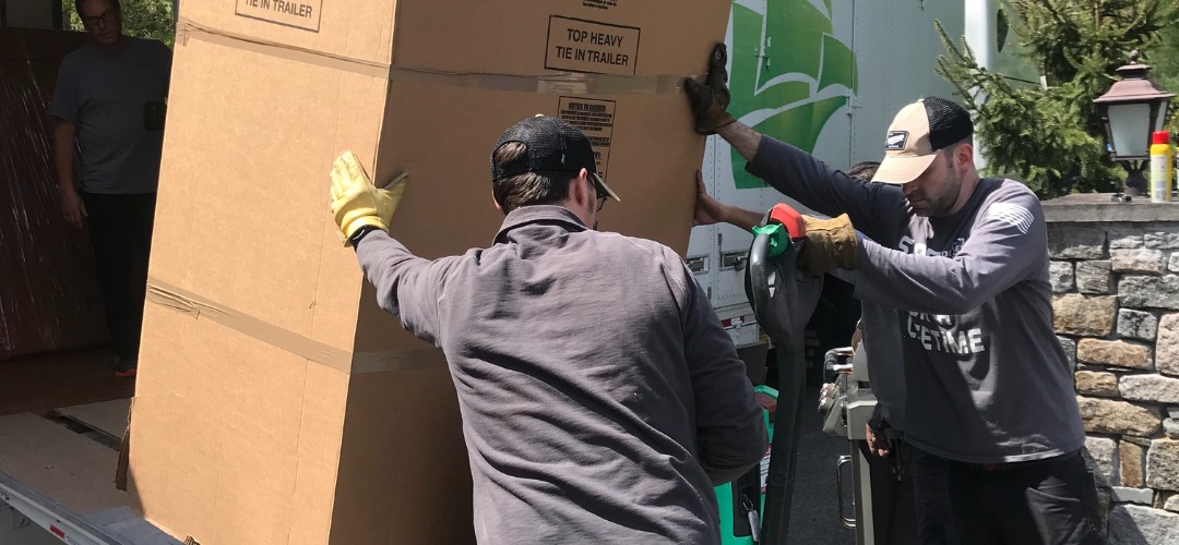 Movers guiding a large cardboard crate onto a truck ramp